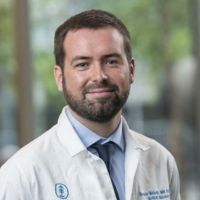 Portrait of a researcher in a lab coat, smiling in an outdoor setting.
